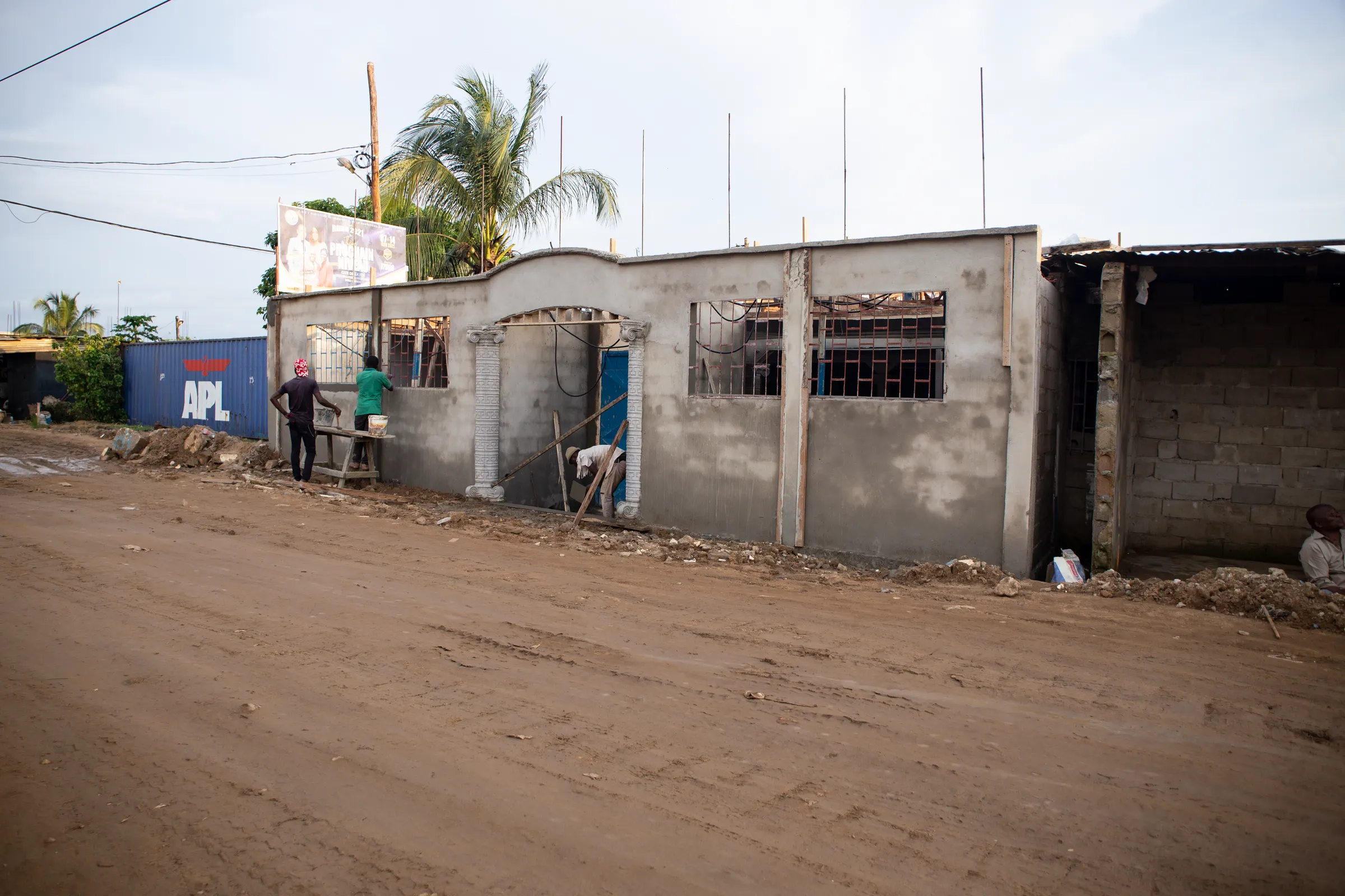 Single-storey cement-block house under construction beside a dirt street