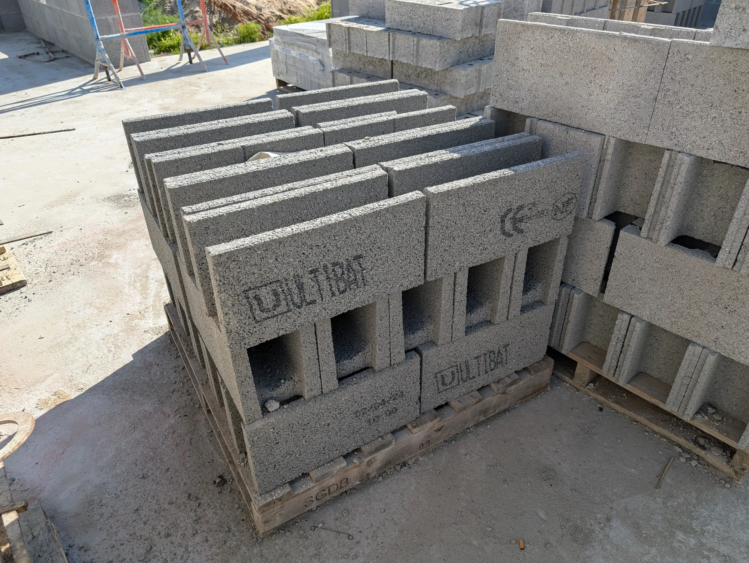 Pallets of new hollow cement blocks on a building site, with sharp corners, clean edges and the maker's certification mark