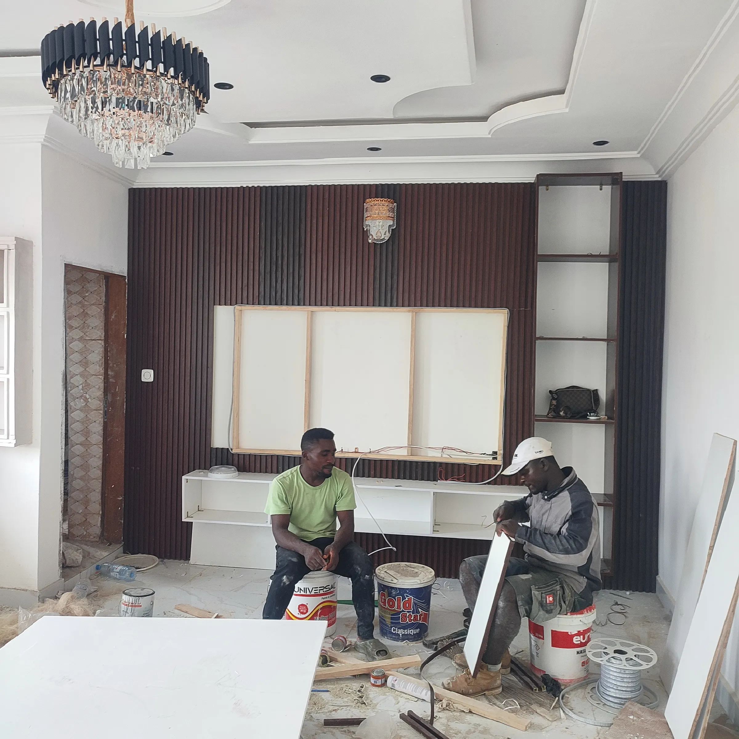 Two FESFAHM workers fitting a TV unit in front of a wood-slat feature wall in a renovated living room