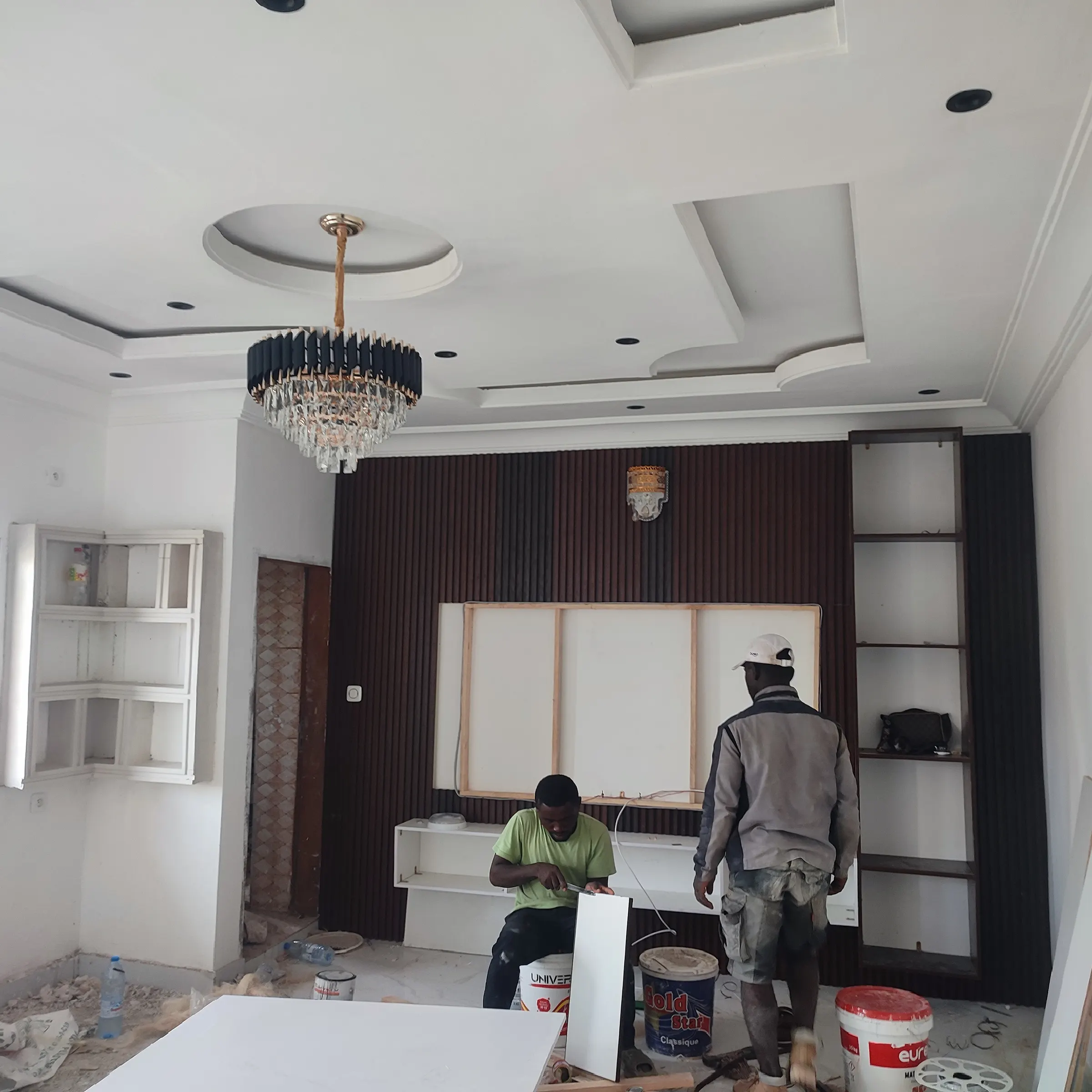 Living room with a layered decorative plaster ceiling, recessed lights and a crystal chandelier, while finishing work continues