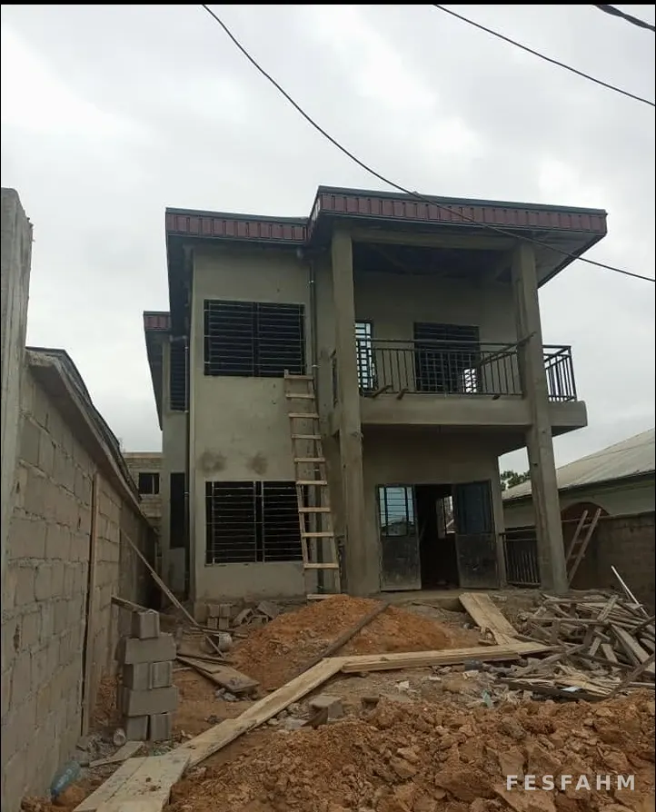 Rendered two-storey house with a balcony, window grilles and a finished roof, with a ladder and timber on site
